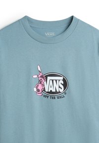 Vaaleansininen puuvillapaita, jossa on vaaleanpunainen pupugrafiikka mustan soikean kuvion vieressä, jossa lukee "VANS OFF THE WALL", pyöreä kaula-aukko ja lyhyet hihat.