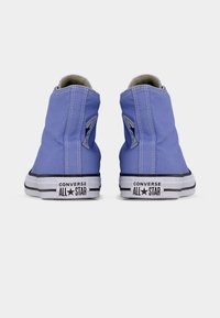 Παπούτσια τύπου ψηλού πάνινου με μπλε καμβά, λευκές σόλες, μαύρες λεπτομέρειες και λαστιχένιο κάλυμμα μύτης. Διαθέτουν ετικέτα με το λογότυπο Converse στο πλάι.