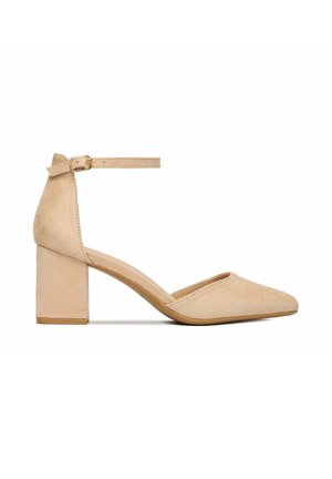 Zapato de tacón ancho para mujer en ante beige con puntera puntiaguda y hebilla en el tobillo, presentado sobre fondo blanco.