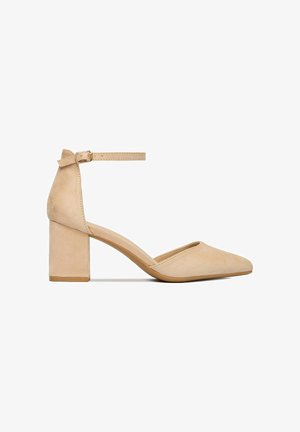 Scarpa da donna beige in camoscio con tacco a blocco, punta appuntita e fibbia alla caviglia, mostrata su sfondo bianco.