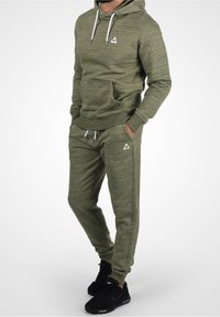Olivgrünes Hoodie- und Jogginghosen-Set aus weichem Material, mit einer Fronttasche, weißen Kordeln und Logodetails auf beiden Teilen.