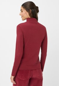 Rotes Langarm-Turtleneck-Shirt aus weichem Stoff, mit taillierter Passform und hohem Kragen. Sichtbare Nähte an den Ärmeln.
