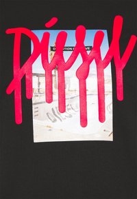 Černé tričko s velkým růžovým grafickým prvkem, na kterém je nápis "Diesel" nad obdélníkovou fotkou skateboardové oblasti s graffiti.