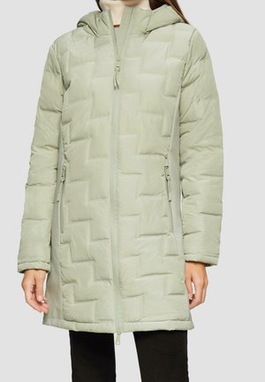 Femme portant un long manteau d'hiver matelassé à capuche vert clair avec une fermeture éclair frontale et des poches latérales zippées.