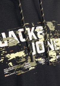 Felpa nera con una grande stampa grafica in bianco e giallo tenue. Presenta un cappuccio con cordini neri e gialli. Tessuto morbido.