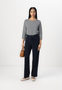 Camiseta de rayas de manga larga, pantalones azul marino ajustados con cintura elástica, zapatos planos beige y un pequeño bolso marrón.