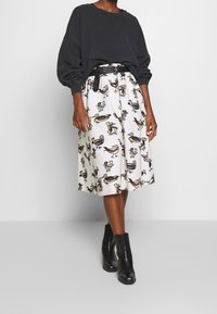 Zwarte oversized trui gecombineerd met een witte midilange rok met een vogelpatroon in zwart en beige. Zwarte enkellaarzen maken de outfit compleet.