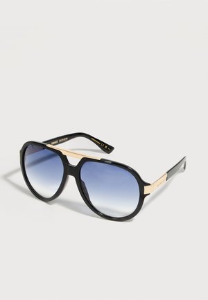 Μαύρα γυαλιά ηλίου aviator με φακούς σε βαθμιαία απόχρωση μπλε και χρυσές λεπτομέρειες στα πλαϊνά και τη γέφυρα της μύτης, τοποθετημένα σε λευκό φόντο.