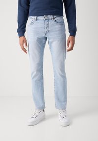 Jean en denim bleu clair avec une coupe droite, cinq poches et une fermeture éclair. Associé à des baskets blanches et un sweat-shirt bleu marine.