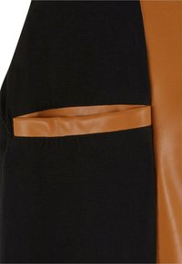Schwarzer Stoff mit einem glatten braunen Kunstlederakzent. Verfügt über eine sichtbare Tasche auf der linken Seite mit kontrastierenden Nähten.