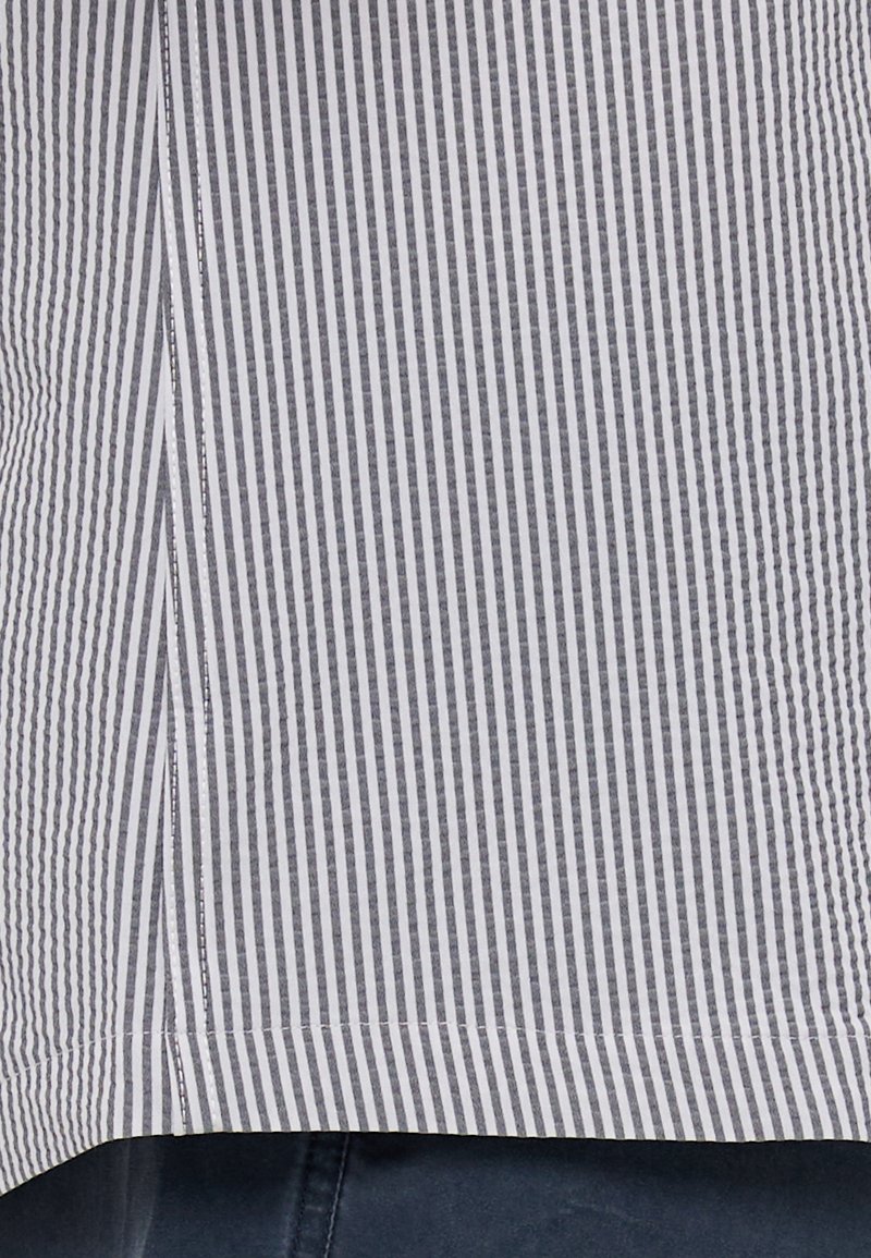 Chemise en coton rayée avec des lignes verticales grises et blanches, ourlet légèrement arrondi, avec des coutures visibles le long des bords.