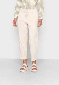 Světlé béžové kalhoty s páskem na stažení v pase. Mají boční kapsy, pohodlný střih a manžety na kotnících. Kombinované s bílými platformovými sandály.