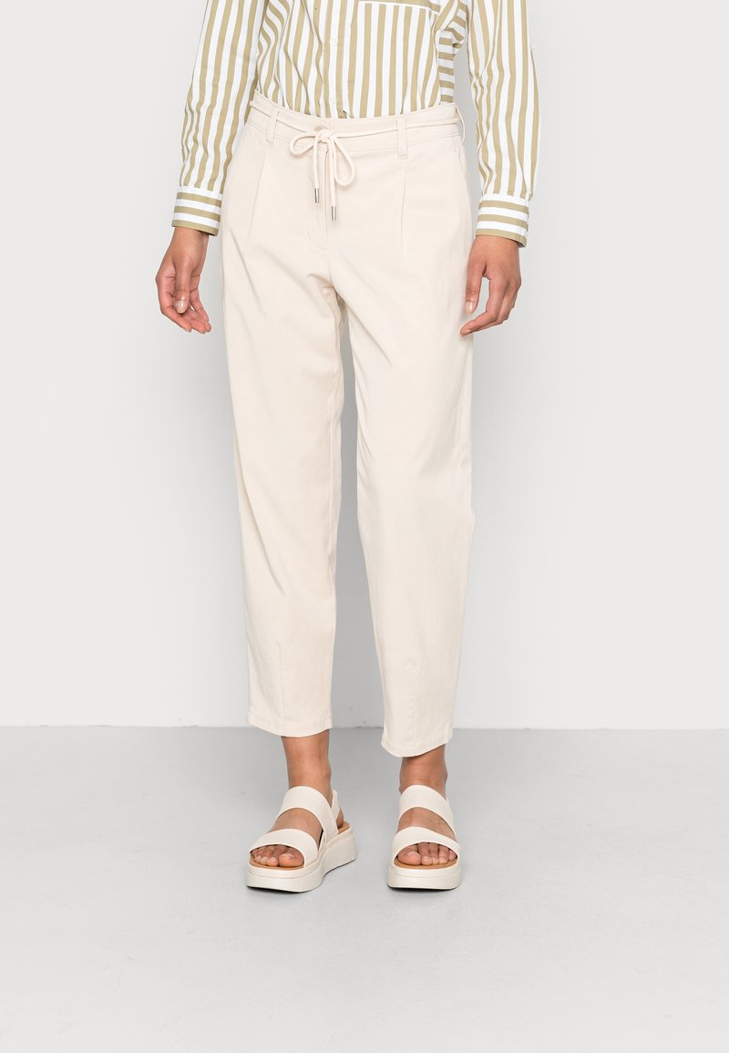 Světlé béžové kalhoty s páskem na stažení v pase. Mají boční kapsy, pohodlný střih a manžety na kotnících. Kombinované s bílými platformovými sandály.