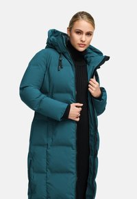 Dolga turkizno modra puhasta jakna s kapuco, ki ima zadrgo, stranske žepe in rebraste manšete. Gladek občutek in izolirano polnilo.