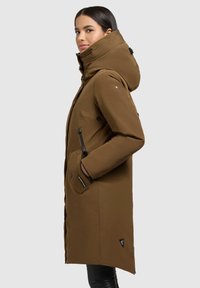 Brun parka med høj krave og hætte, der har lynlåslommer og et diskret logo. Stoffet ser glat og vandafvisende ud.
