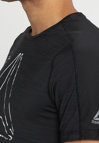 Black athletic t-shirt with a fitted design, featuring a textured surface and white sailboat graphic on the front. Logos on sleeve.