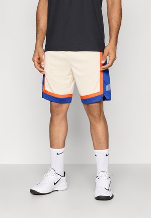 Shorts de sport pour homme en crème avec des accents bleus et oranges, présentant un design en maille et des détails rayés sur les côtés. Portés avec des chaussettes et des chaussures blanches.