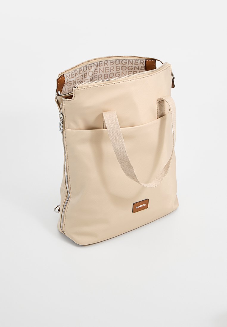 Beige Tote-Bag aus glattem Material, mit Reißverschluss, zwei Tragegriffen und einer Vordertasche mit einem gebrandeten Lederpatch.