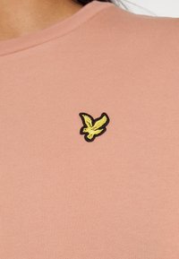 T-shirt a righe rosa chiaro con logo di un uccello ricamato in nero e giallo sulla parte sinistra del petto. Maniche corte, scollatura tonda.