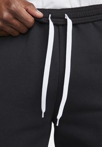 Svarta mjukisbyxor med elastisk midjeband, utrustade med vita dragsnören, slät textur och en närbild av midjeområdet.