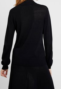 Schwarzer Strickpullover mit geripptem Kragen und Bündchen, lockerer Passform und strukturierten Details auf dem Rücken und denÄrmeln.