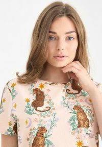 Růžové tričko s krátkým rukávem s leopardím potiskem a květinovým vzorem, se zelenými listy a dekoračními hvězdami v různých barvách.