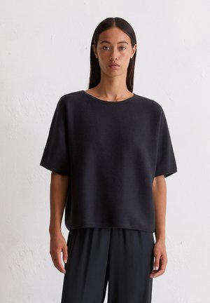 Black oversized T-shirt made of textured fabric with a round neckline and short sleeves, paired with loose-fitting dark trousers.
