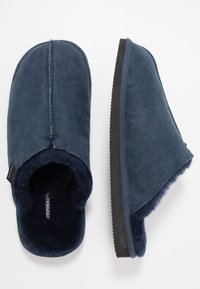 Marineblå hjemmesko lavet af blødt suede med uldfoer, med lukket tå, åben ryg og en struktureret sort gummisål.