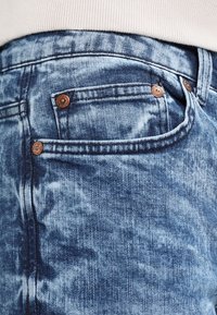 Jeans in denim blu sbiadito con una texture consumata, dotati di due bottoni metallici visibili e di una tasca laterale.
