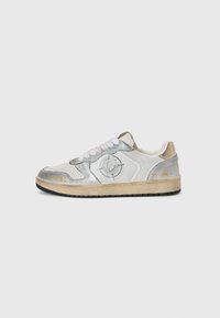 Silberne und weiße Sneakers mit einem eleganten Design, das strukturierte Materialien, ein rundes Logo-Detail, eine schwarze Sohle und metallische Akzente umfasst.
