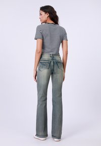 Lichtblauwe uitlopende jeans met een vervaagde textuur, twee achterzakken en een hoge taille, gecombineerd met een zwart-wit gestreept t-shirt.