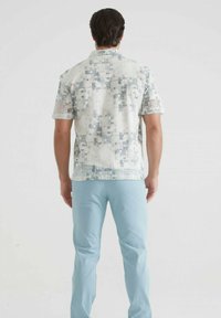 Chemise à manches courtes de couleur claire avec une texture motif en nuances de bleu, associée à un pantalon bleu pastel pour un look décontracté.