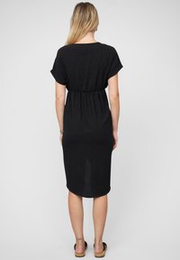 Black dress made of lightweight fabric, featuring short sleeves, elastic waist, and a knee-length design with a curved hem.