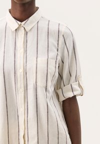 Linned skjorte i off-white med vertikale brune striber, krave med opbrettede ærmer, med en frontlomme og knaplukning.
