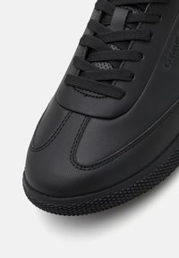 Czarne trampki z teksturowaną skórzaną cholewką, płaskimi sznurowadłami i gumową podeszwą z wzorzystym gripem. Gładkie wykończenie z zaokrąglonym czubkiem.