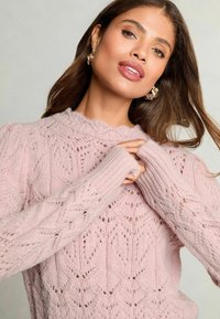 Maglione lavorato a maglia di un rosa chiaro con un motivo testurizzato a foglia, polsini a coste e scollatura ondulata, caratterizzato da maniche lunghe.