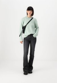 Pull à côtes vert menthe clair, jean noir évasé et chaussures noires. Le pull a des manches longues et un col rond, porté avec un petit sac noir.