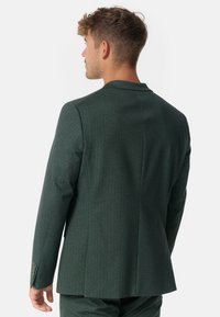 Dunkelgrüne Anzugsjacke im Fischgratmuster mit Revers, zwei Knöpfen und feiner Textur, von hinten betrachtet.