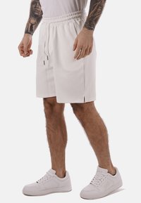 Shorts bianchi con vita elasticizzata e coulisse, fessure laterali e tessuto morbido e strutturato. Abbinati a sneakers bianche.
