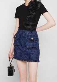 T-shirt noir avec des détails en soie froncée, associé à une mini-jupe en tweed bleu comportant deux grandes poches et des boutons dorés.