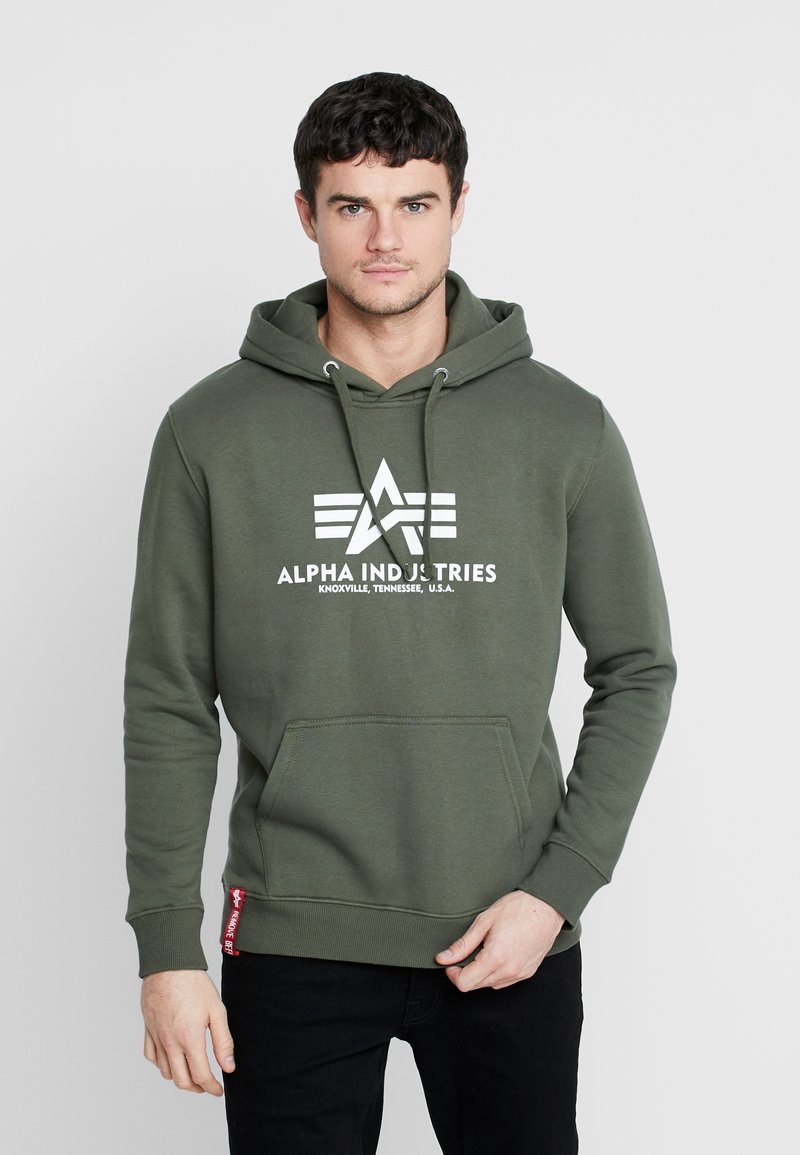 Groene katoenen hoodie met wit Alpha Industries-logo en sterren. Heeft een kangoeroezak en ribgebreide boorden bij de mouwen en taille.