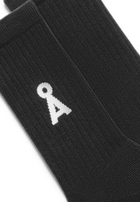 Sorte sokker med et hvidt bogstav "A" logo. Strikket tekstur med et ribbet mønster, der giver en tætsiddende pasform omkring ankel og fod.