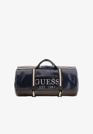 Borsa duffle Guess blu navy e marrone con rifiniture bianche, tasca frontale con zip, scritta del logo "GUESS EST. 1981" e doppi manici con tracolla a righe.