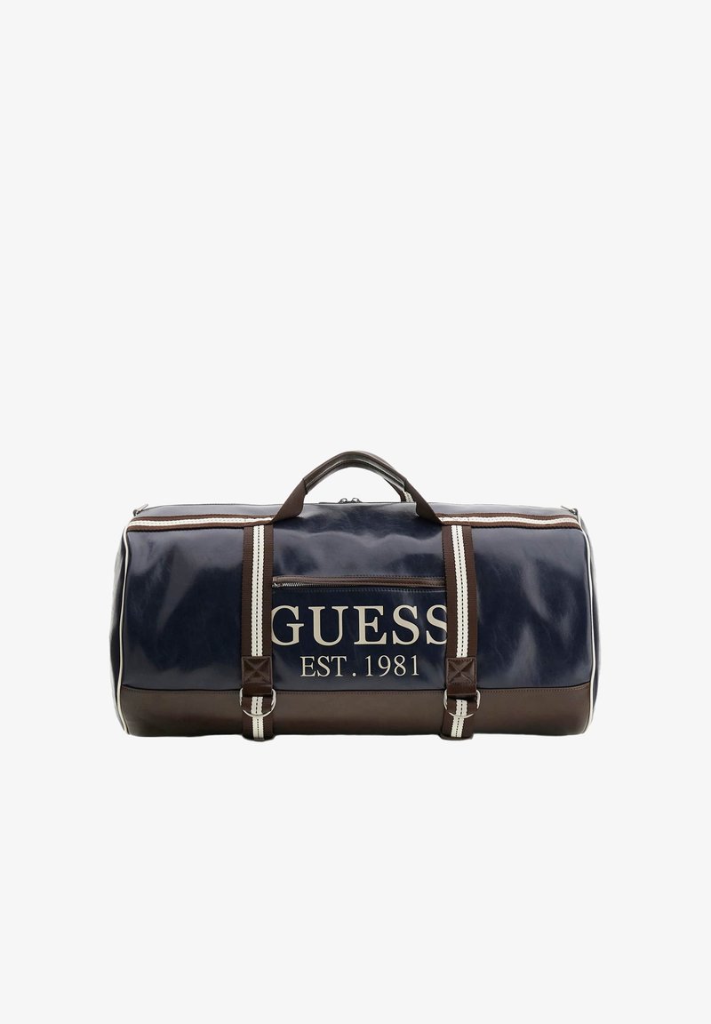 Sac duffle Guess bleu marine et marron avec bordure blanche, poche avant zippée, texte du logo "GUESS EST. 1981" et doubles poignées avec bandoulières rayées.