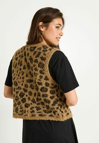 Chaleco de estampado de leopardo marrón hecho de una tela texturizada con un diseño corto. Lleva encima una camiseta de manga corta negra, con un dobladillo recto.