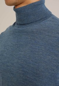 Blå turtlenecktröja med ribbat krage och ett mjukt, texturerat tyg. Närbild som framhäver stickmönstret och färgvariationerna.