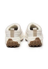 Zapatillas blancas con parte superior texturizada, que cuentan con aberturas elásticas y suelas de goma marrón. Con lengüetas traseras para facilitar el calzado.