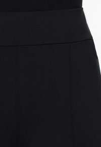 Schwarze hochtaillierte Hosen mit glatter Textur, ausgestattet mit einem breiten Bund und seitlichen Eingrifftaschen. Der Stoff wirkt dehnbar und leicht.