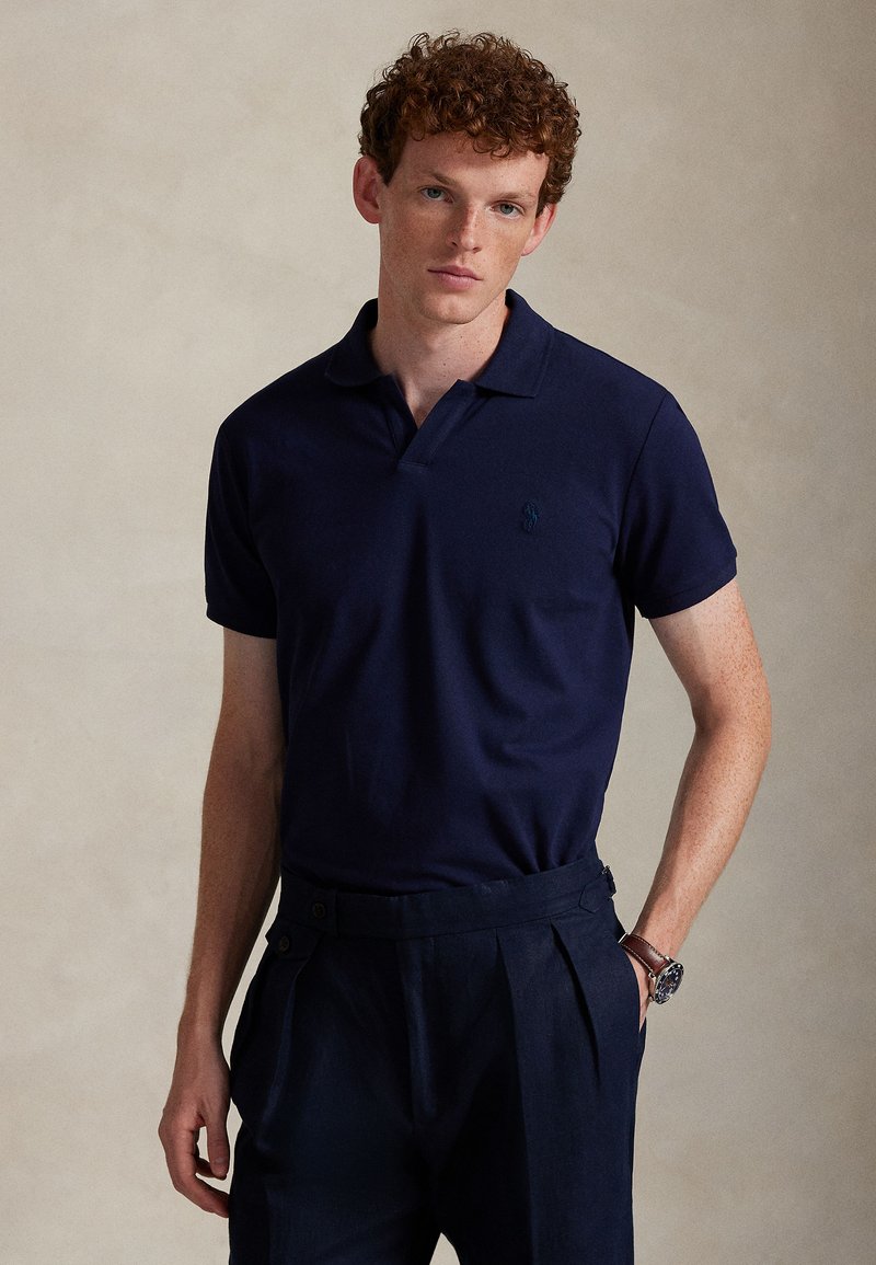 Navy short-sleeve polo shirt in soft fabric, featuring a collar and a small, embroidered logo on the chest. Paired with tailored dark pants.