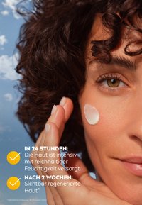 Feuchtigkeitsspendende Creme auf der Wange aufgetragen, mit sichtbarer glatter Haut. Das Model hat lockiges braunes Haar und steht vor einem blauen Himmel.